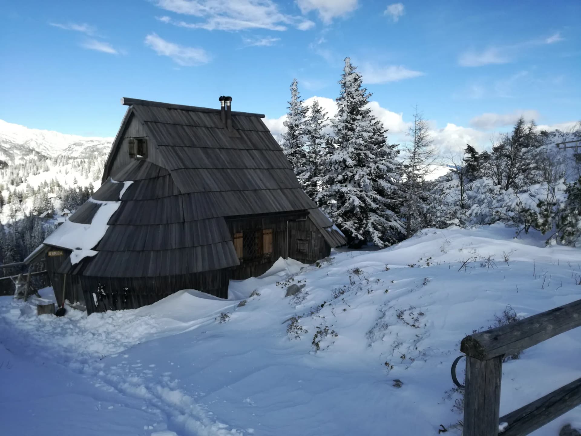 Die Hütte Krnica im Winter, ein Holzhaus mit Schindeldach zwischen verschneiten Fichten