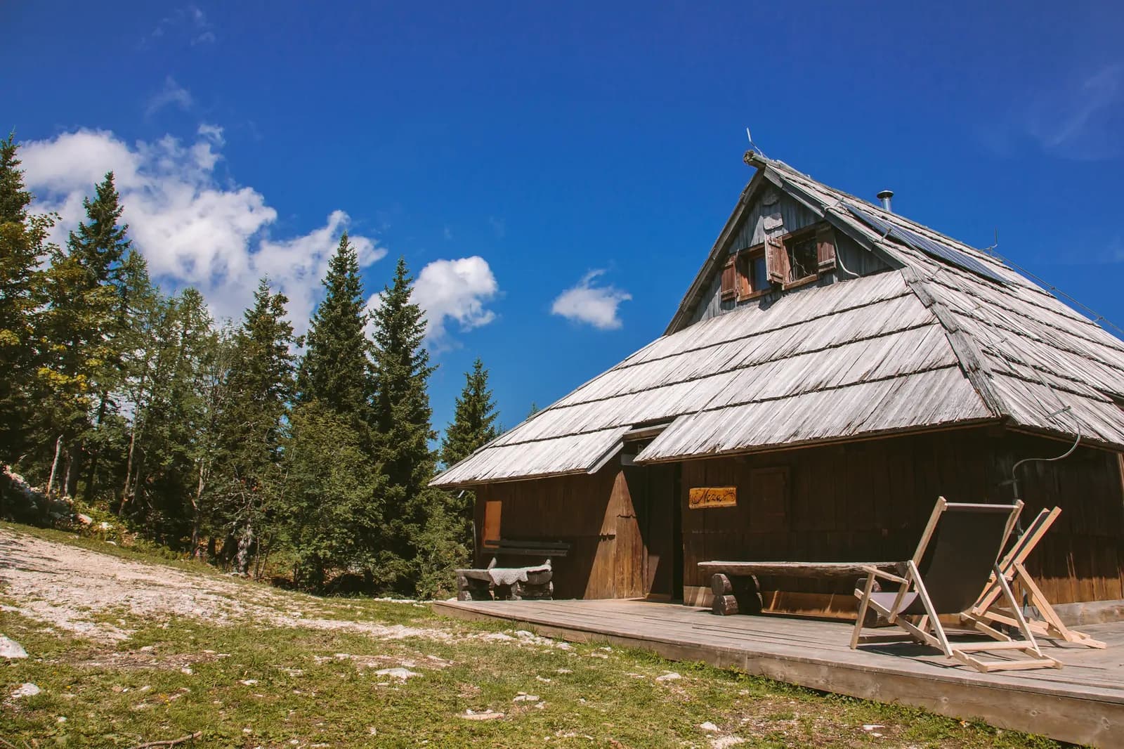 Pastirska koča Neža na travniku Velike planine pod modrim nebom z oblaki
